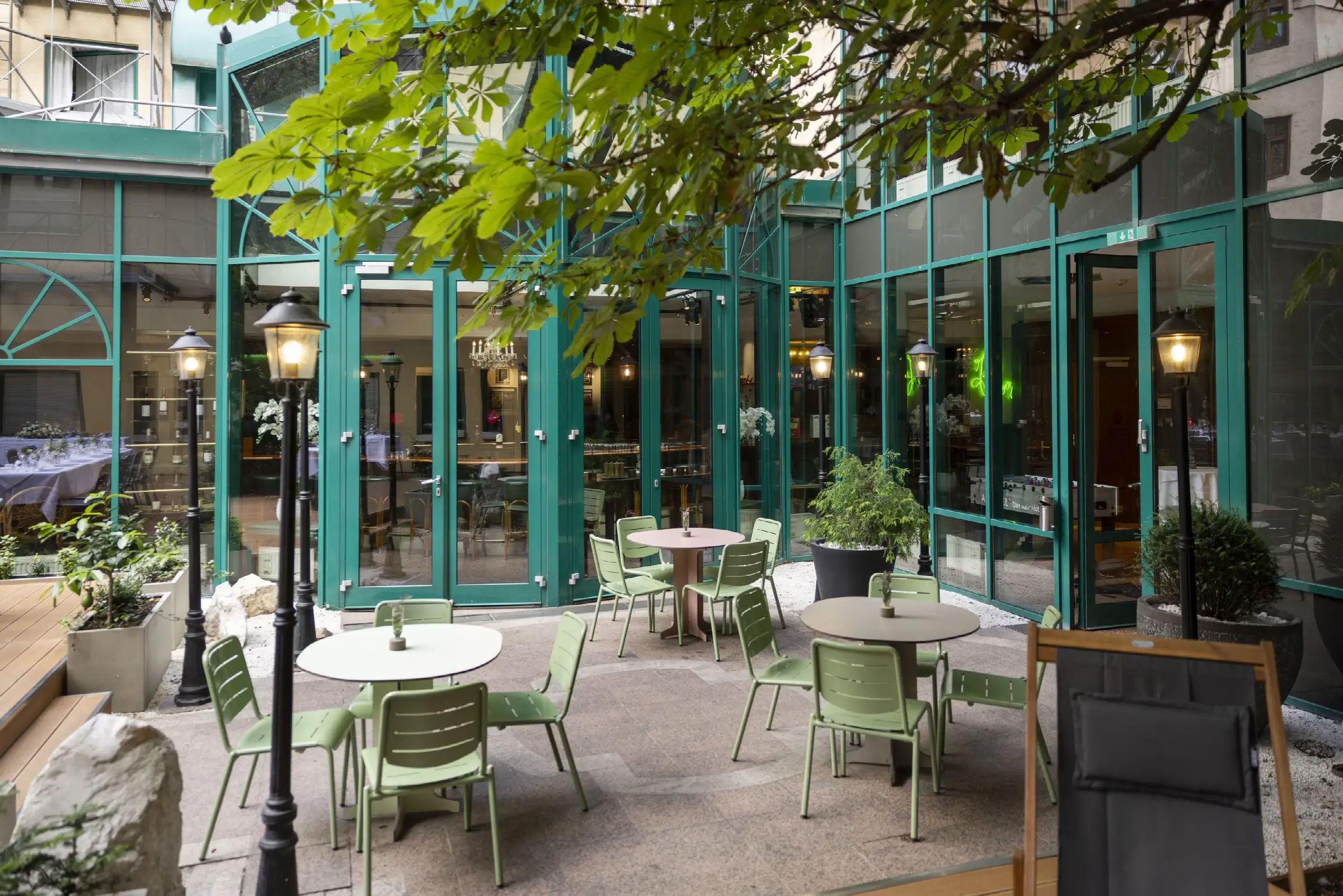 Gemütliche Terrasse im Restaurant mit Tischen und Stühlen, umgeben von Pflanzen und Laternen.