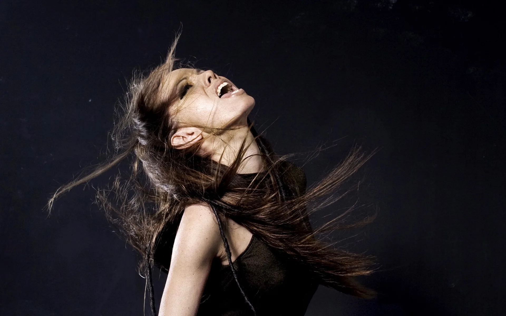 A woman with long, flowing hair in a dynamic pose against a dark background.