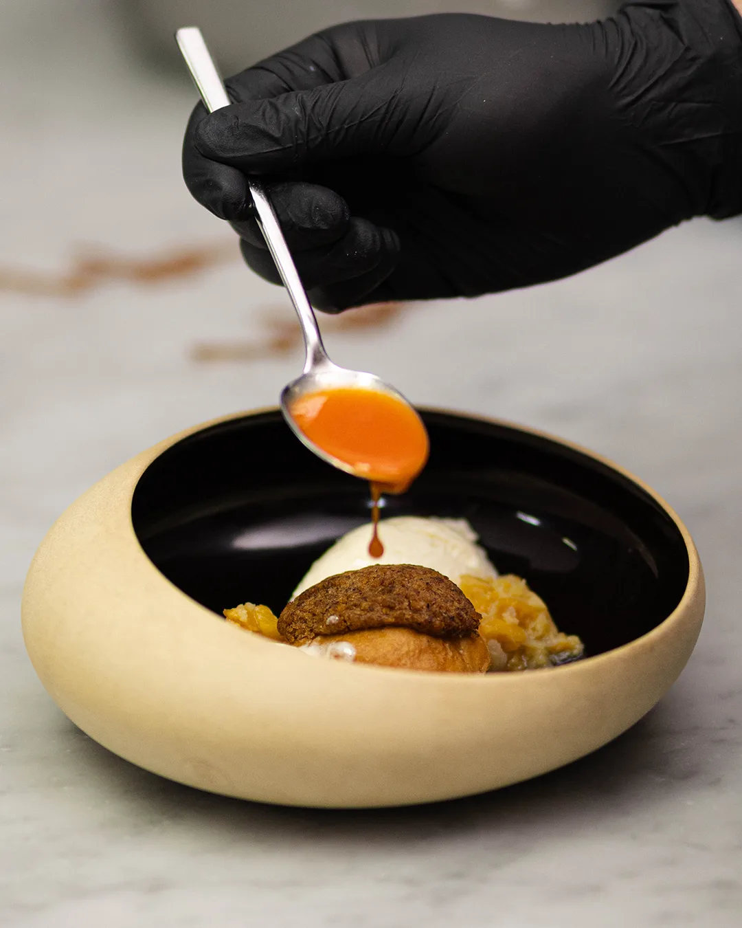 A dessert in a bowl with ice cream, a cookie topping, and an orange sauce.