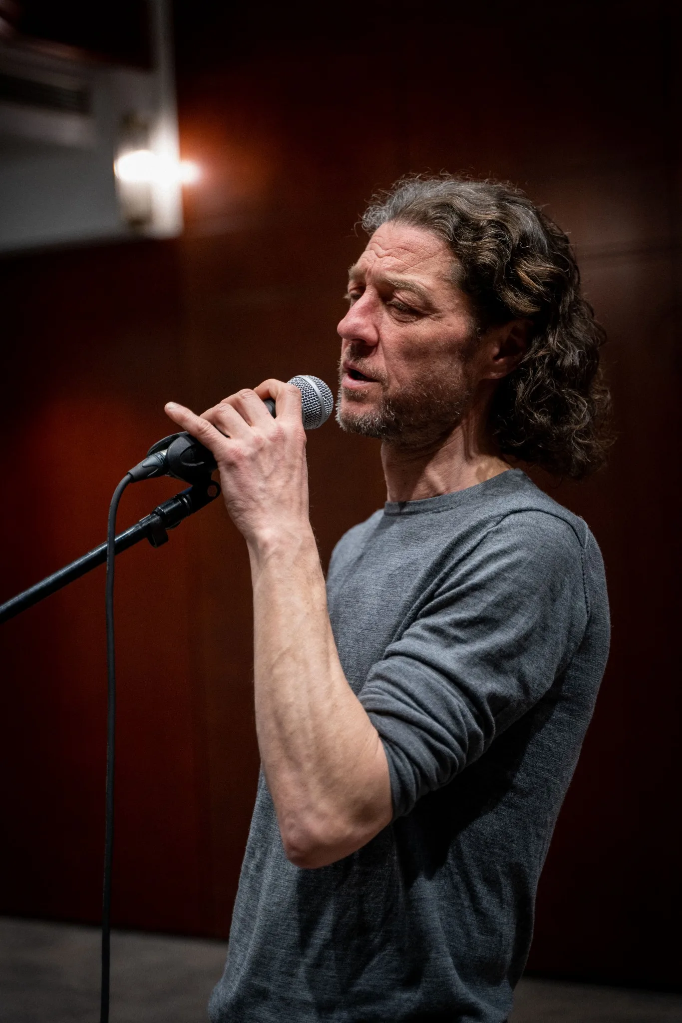 A man with curly hair singing into a microphone on stage.
