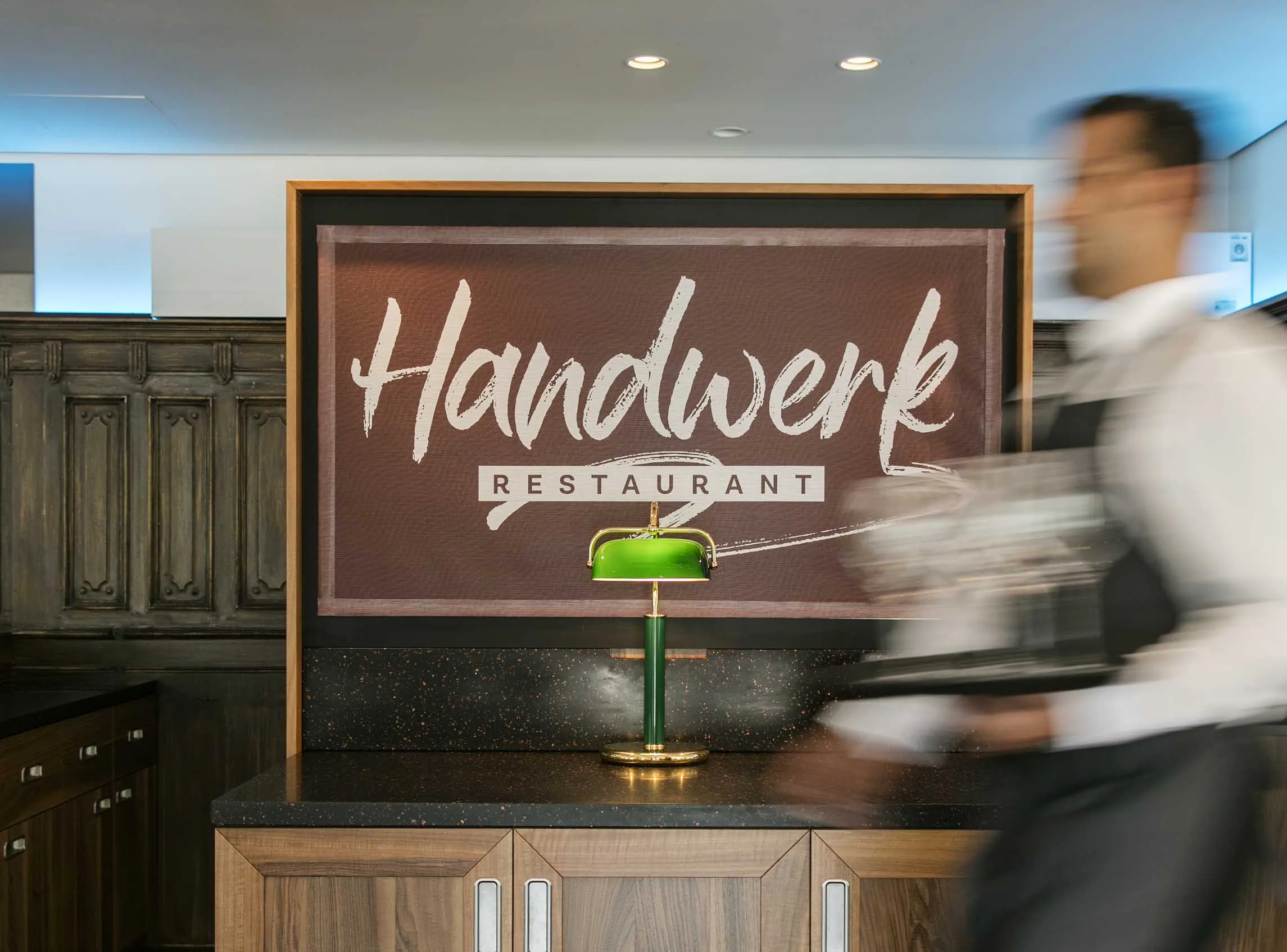 The entrance area of the Handwerk restaurant with a green table lamp and a blurred waiter.