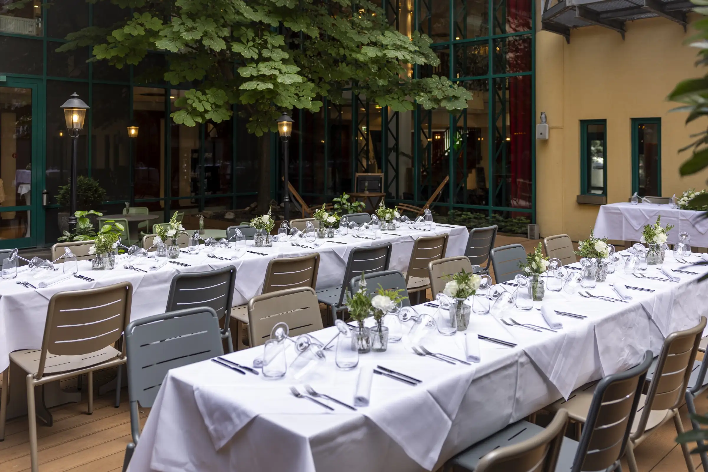 Festlich gedeckter Tisch im Außenbereich des Restaurants mit weißen Tischdecken, Gläsern und Blumen in Vasen.
