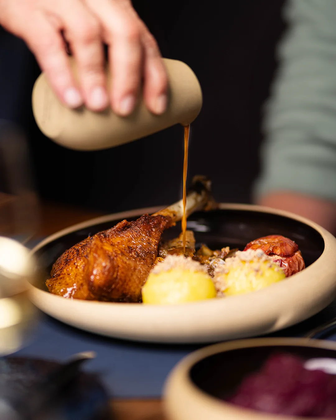 A goose is being drizzled with sauce, served with sides.