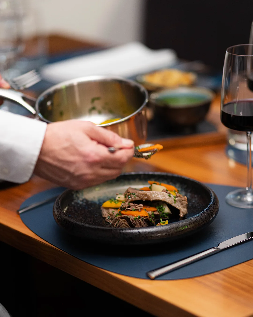 A waiter serves a dish with meat and vegetables.