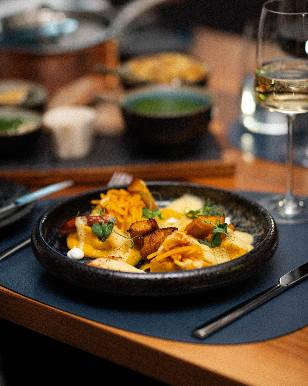 A gourmet dish artfully arranged on a black plate, surrounded by other dishes.