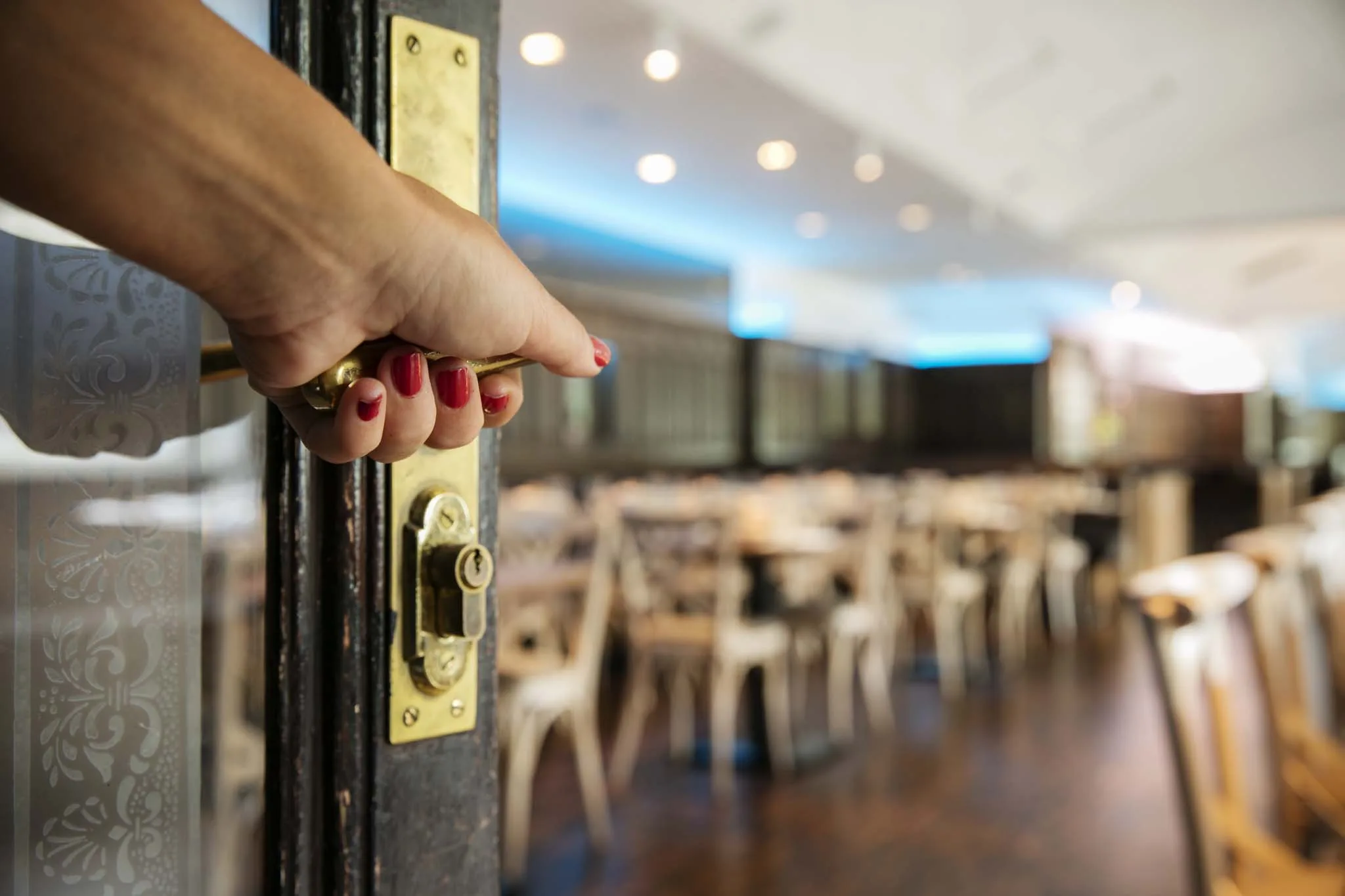A hand opening a door to a restaurant with tables in the background.