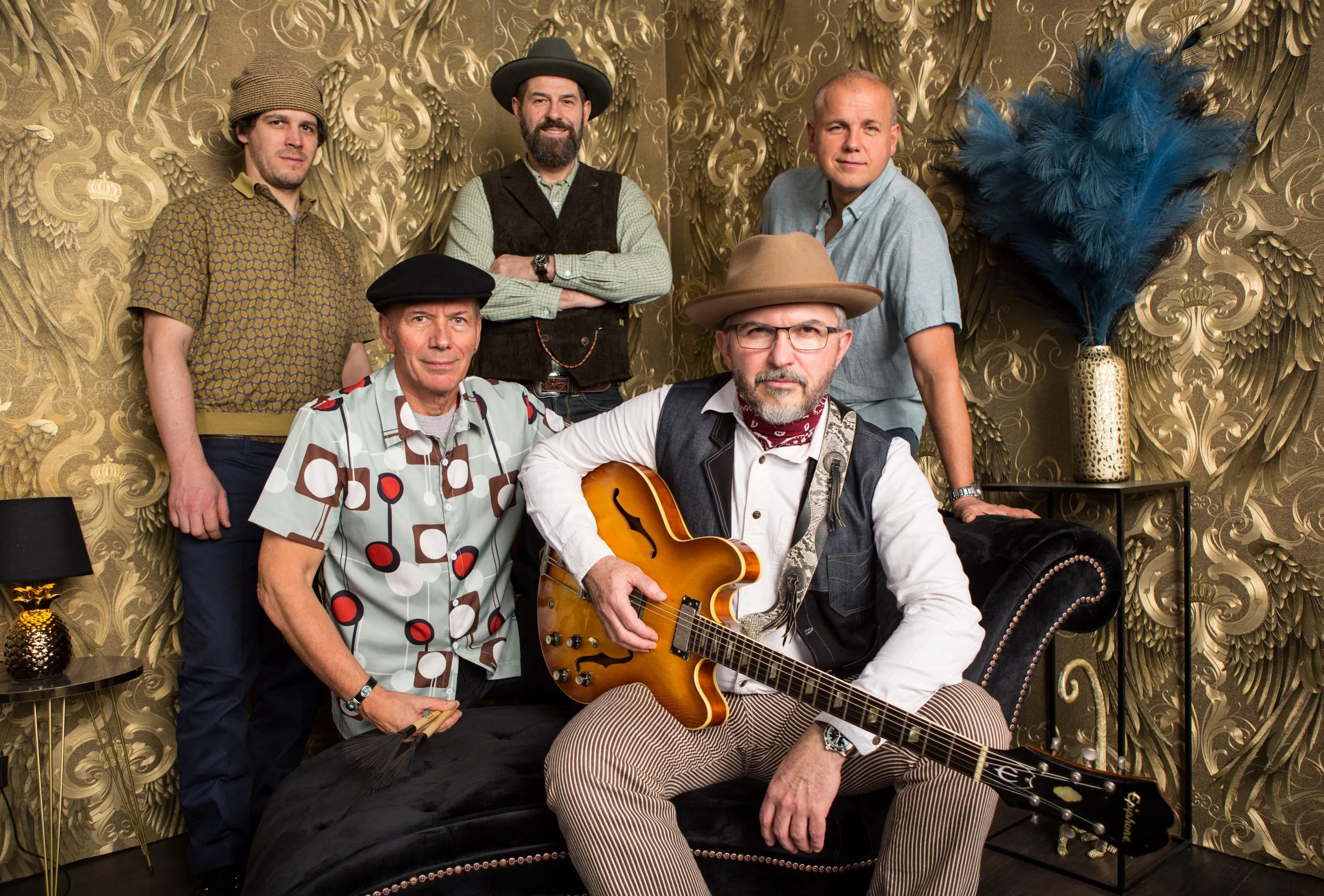 Five musicians posing in a stylish setting with instruments.