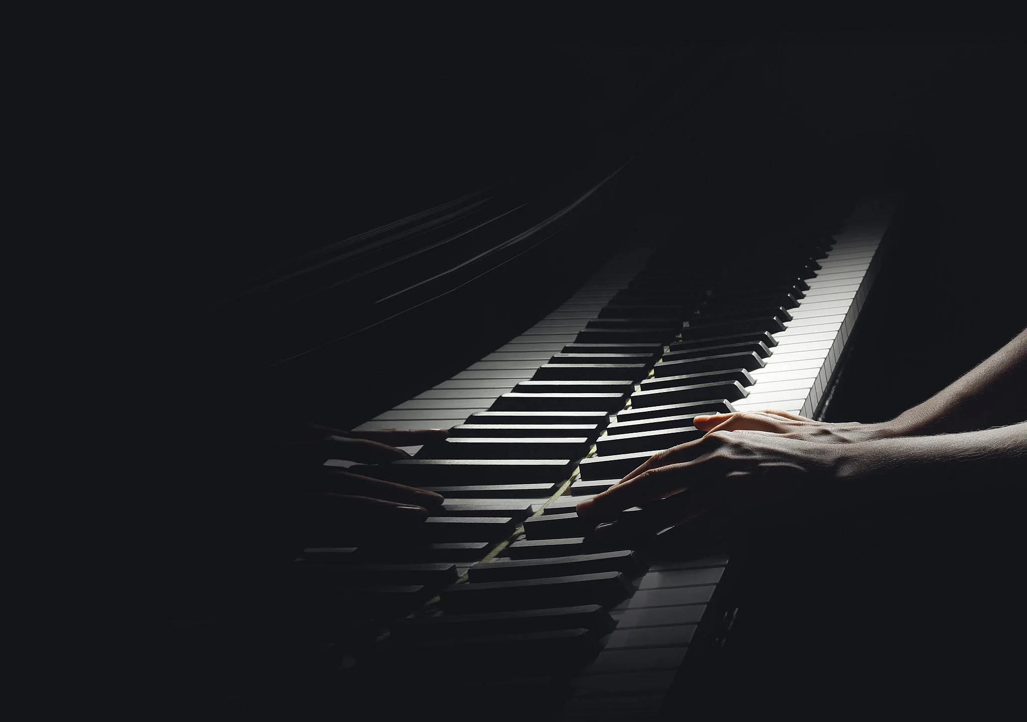 Eine Hand spielt auf den Tasten eines Klaviers in dunkler Umgebung.