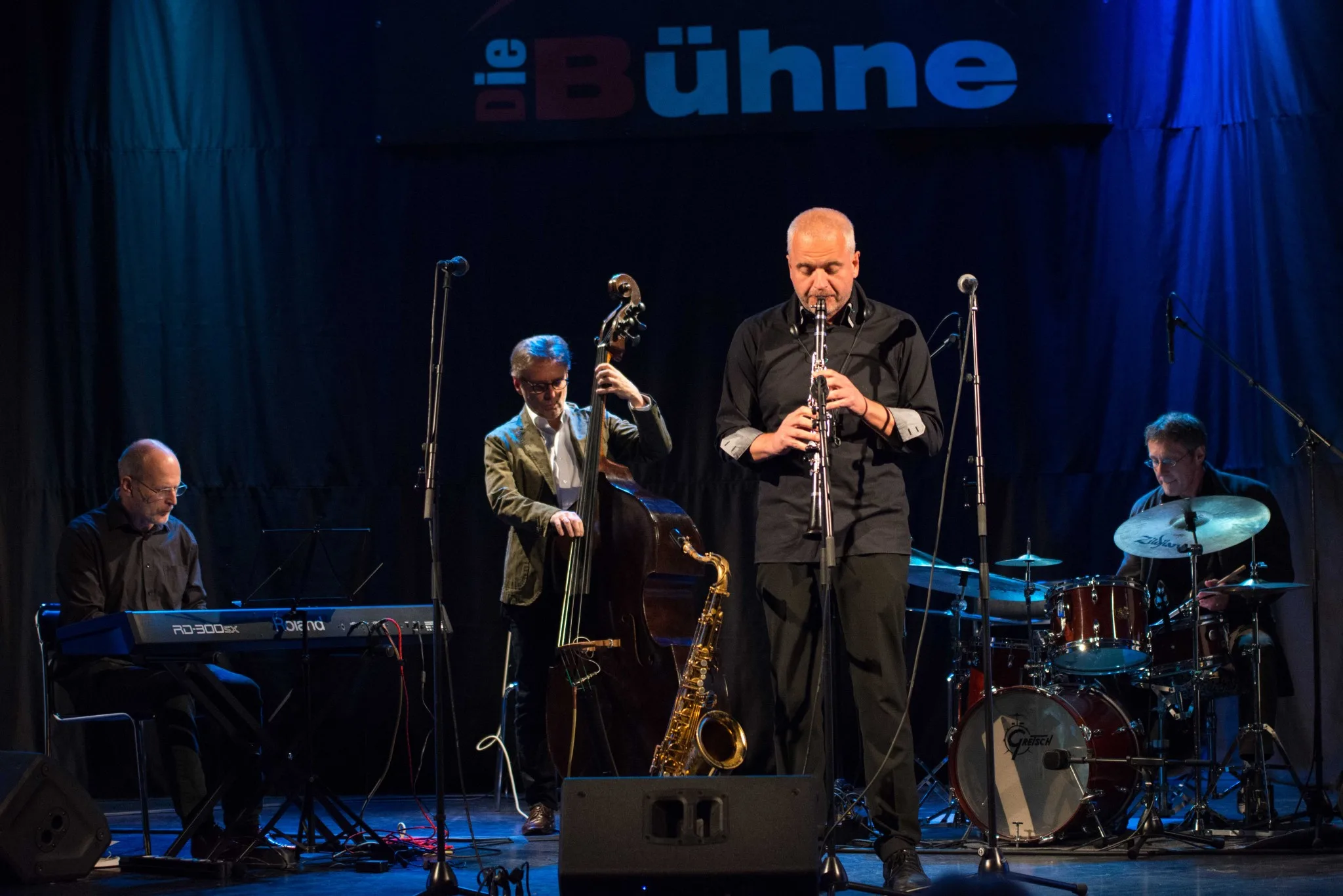 A jazz band performing live on stage with piano, double bass, clarinet, and drums.