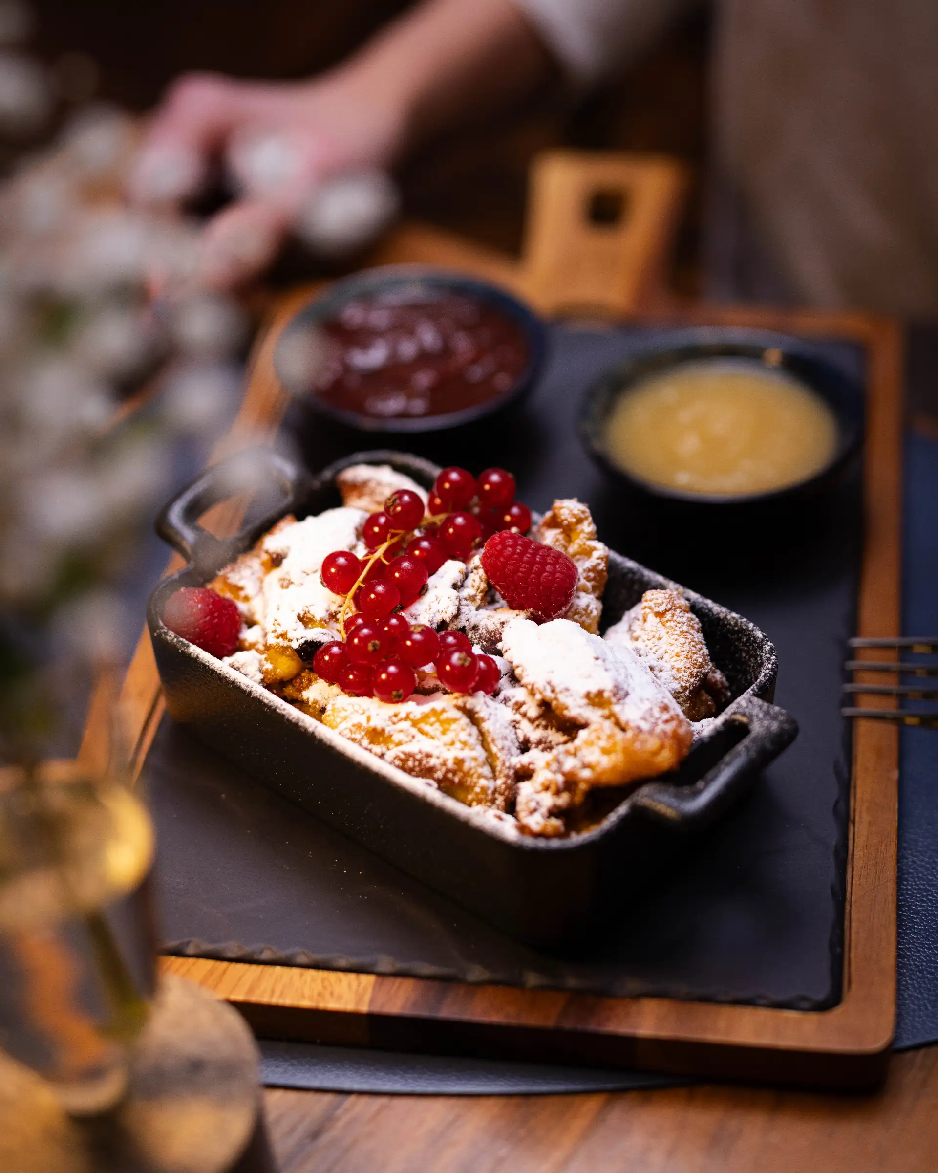 Kaiserschmarrn with powdered sugar, fresh berries, and sauces in a black bowl, served in the restaurant.