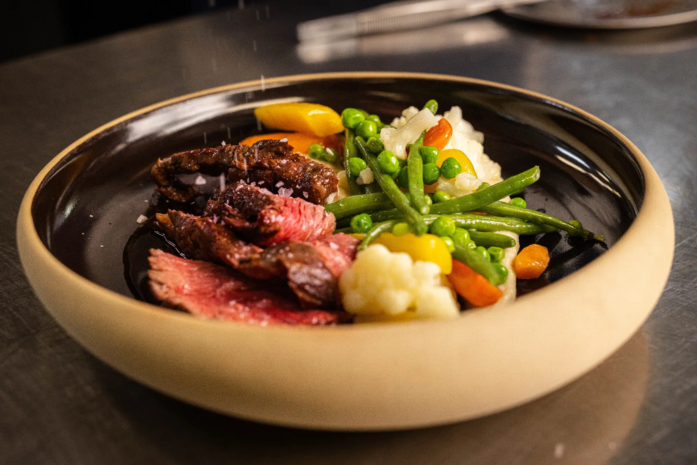 Zartes Rindfleisch mit buntem Gemüse und Beilagen auf schwarzem Teller im Restaurant