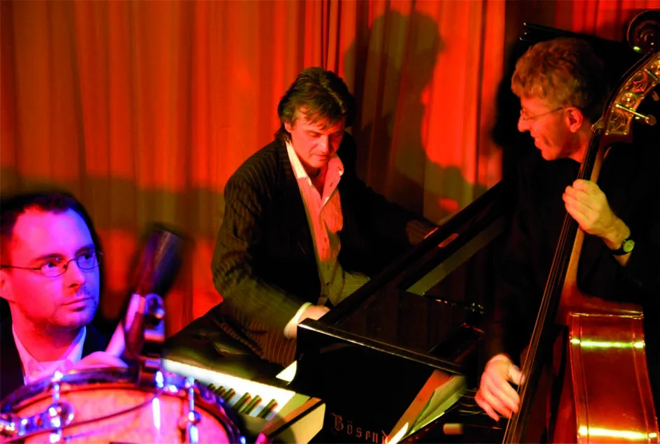 Three musicians performing in a jazz club with red lighting.