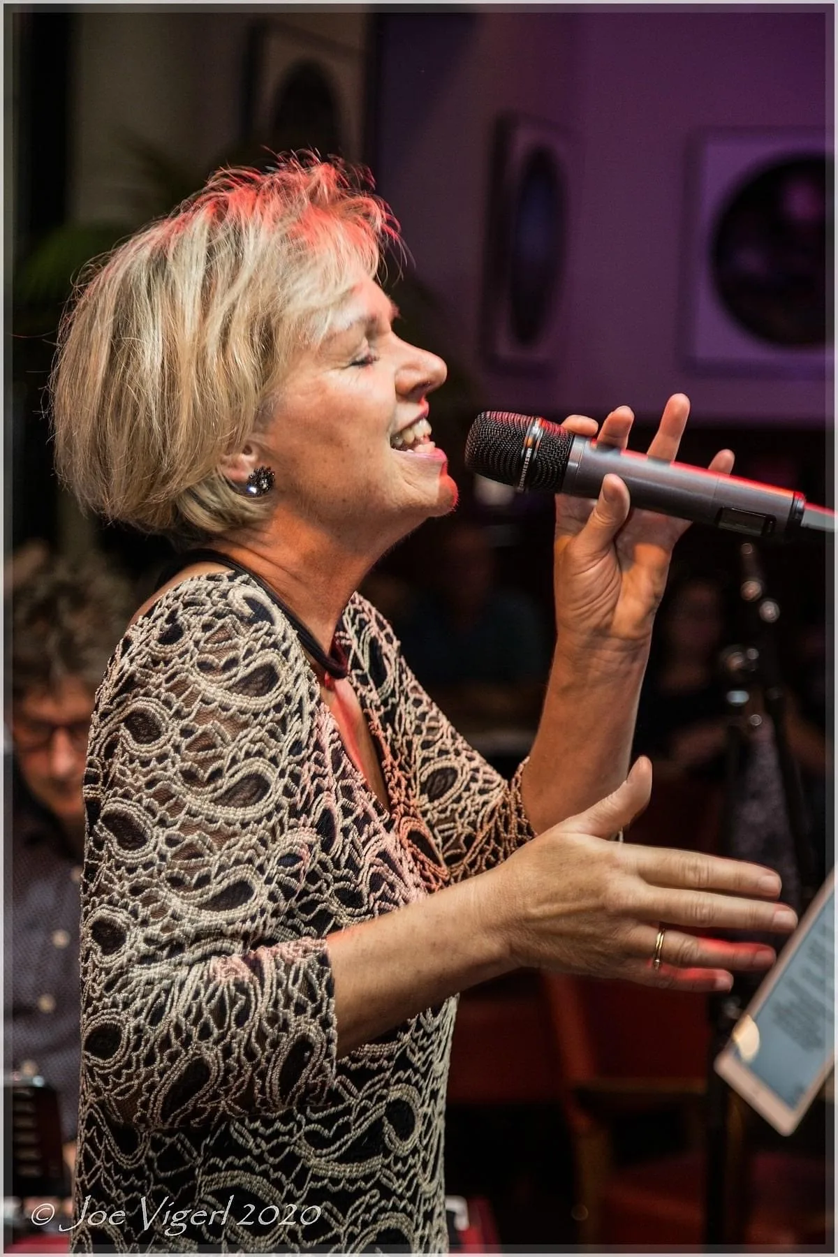 A singer with short blonde hair passionately singing into a microphone.