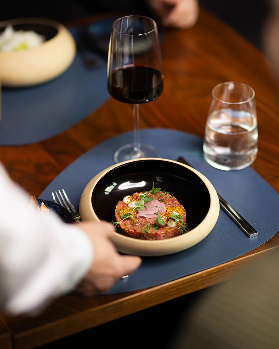 A plate with a gourmet dish and a glass of red wine on a table.
