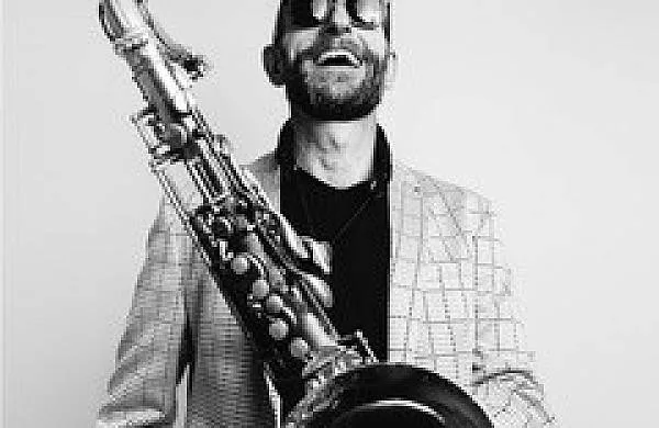 A cheerful man with sunglasses holding a saxophone.