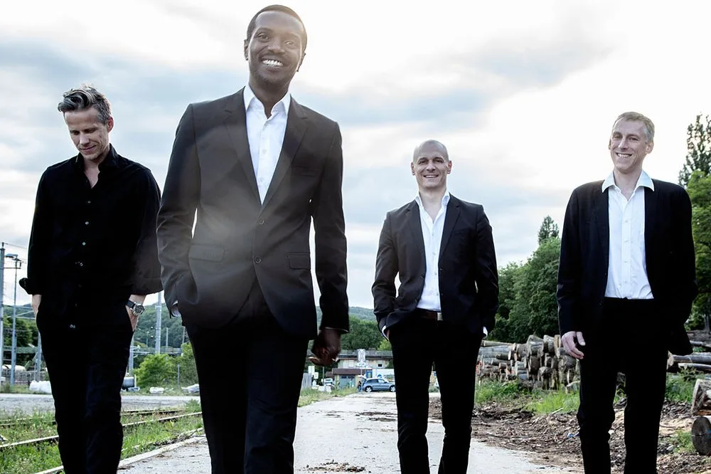 Vier Männer in eleganten Anzügen gehen lächelnd auf einem Weg.