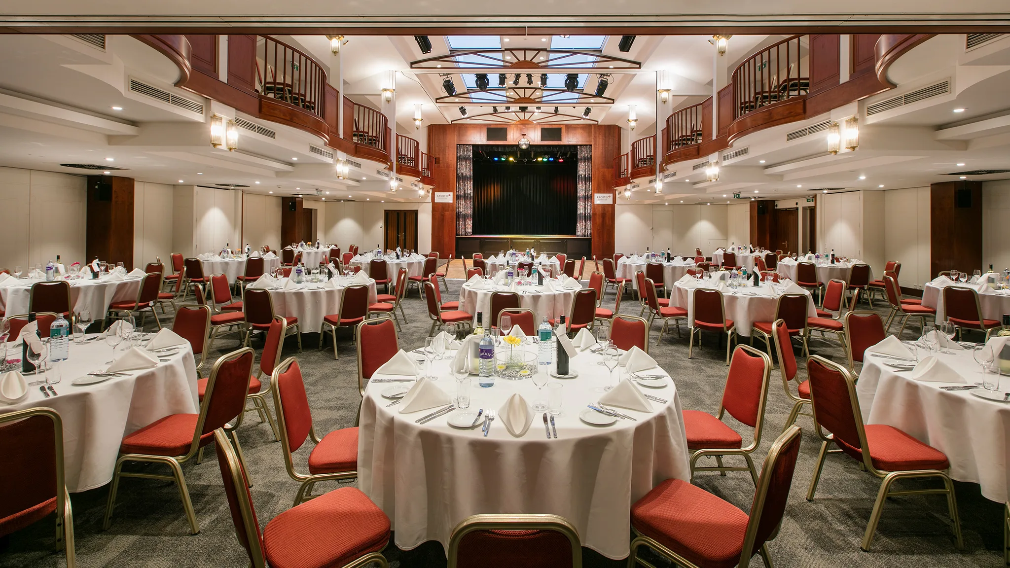 Ein eleganter Veranstaltungsraum mit runden Tischen und rotem Stuhl, bereit für eine Feier.