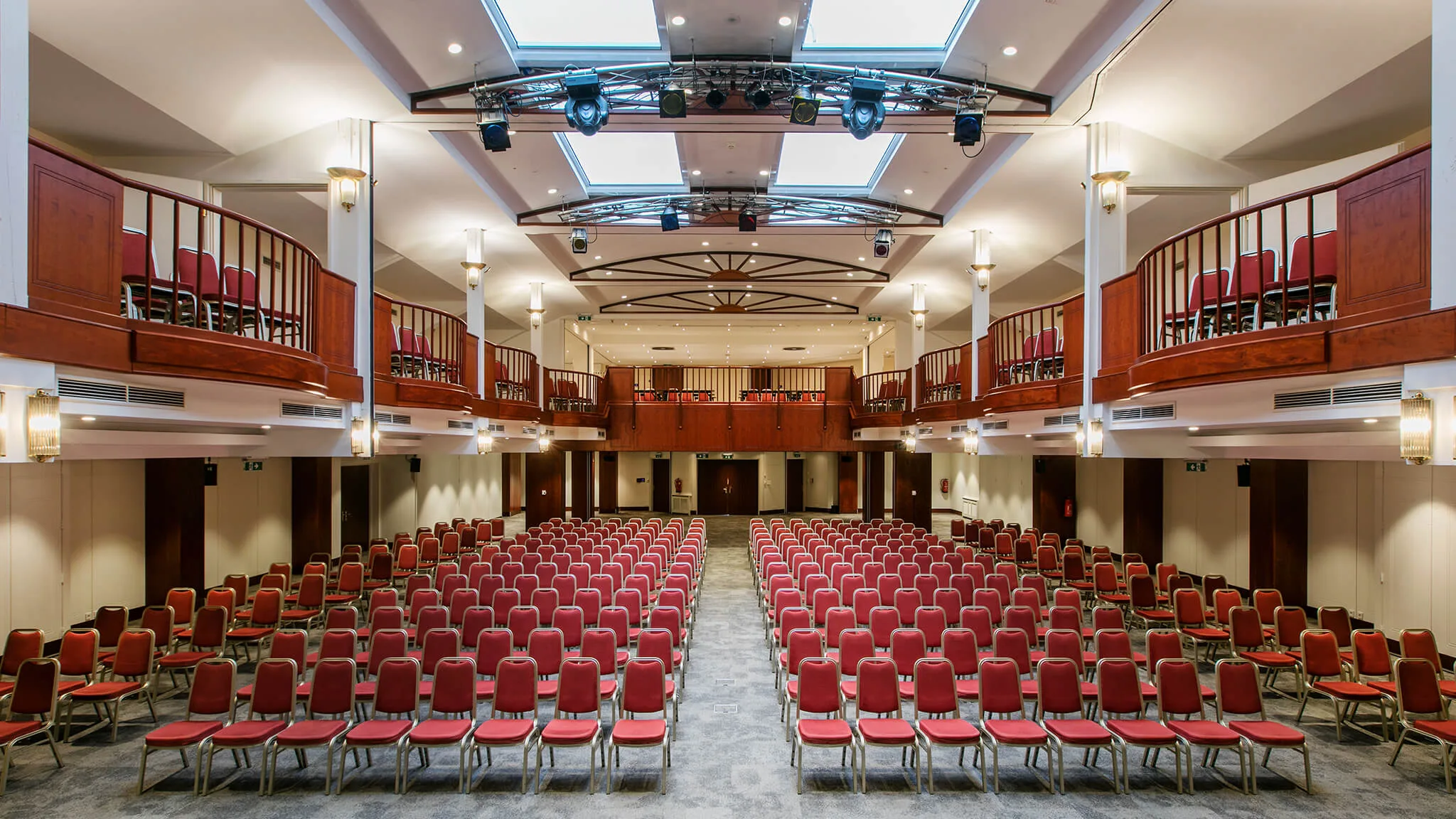 Großer Veranstaltungssaal mit roten Stühlen und Balkon.