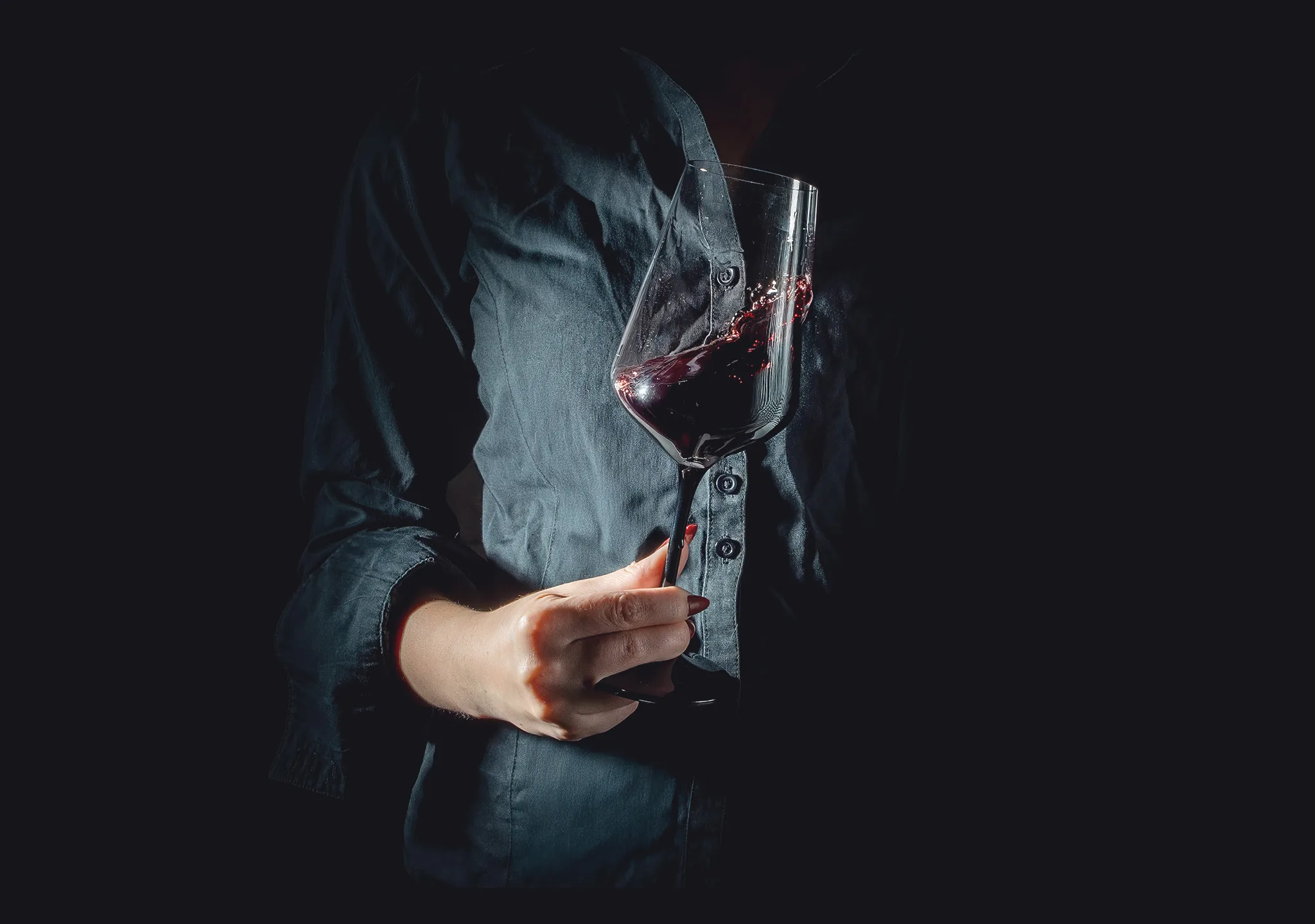 Eine Hand hält ein Weinglas mit spritzendem Rotwein.