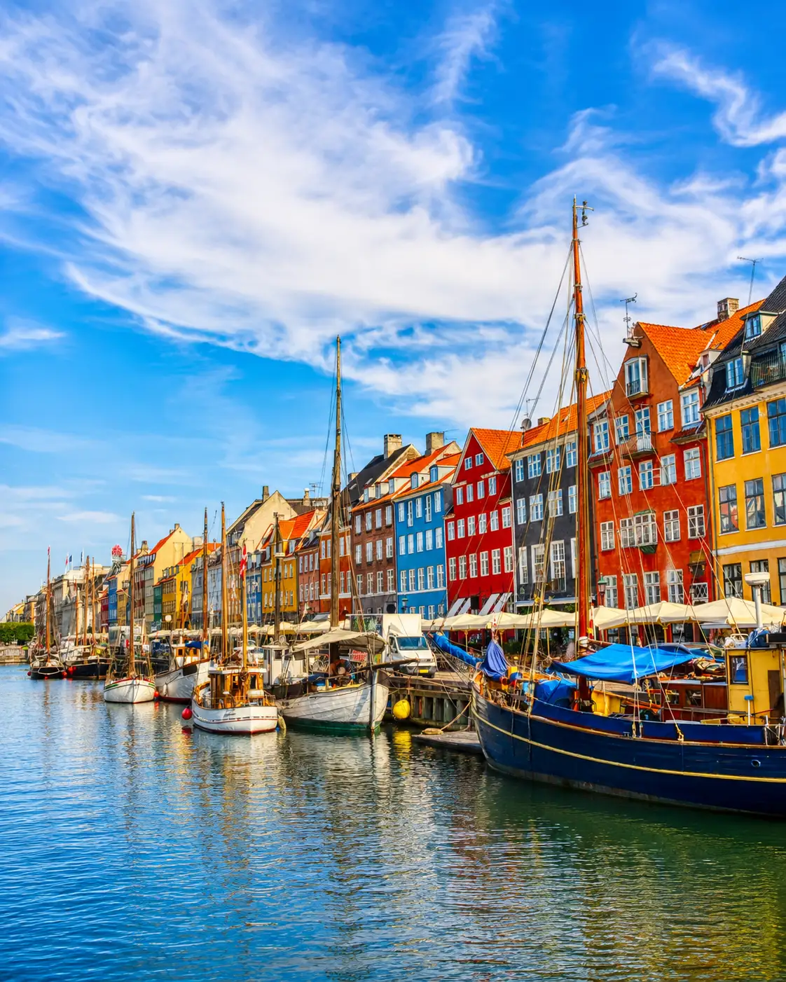 Bunte Häuser am Kopenhagener Hafen mit historischen Booten und klarem Himmel.